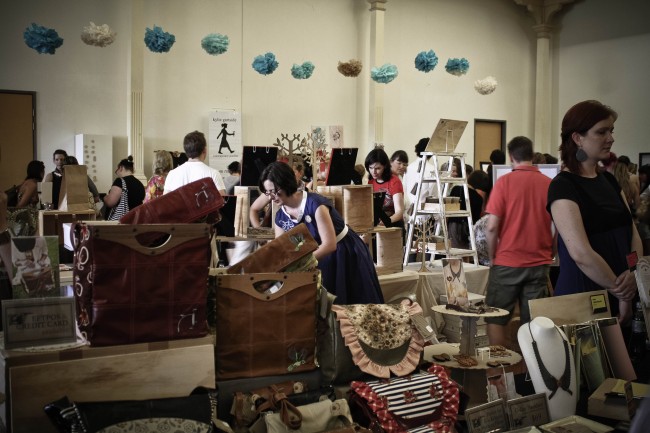 Photo of a hand bag stall in the middle of a large room amongst lots of other crafty stalls and shoppers.