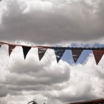 Photo of colourful fabric bunting strung up outside against large white clouds in a blue sky.