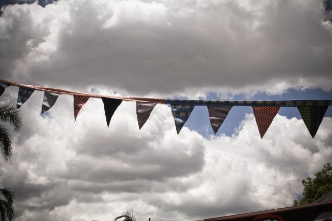 Photo of colourful fabric bunting strung up outside against large white clouds in a blue sky.