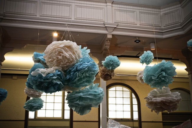 Photo of large blue, cream and fawn pom poms hanging from the ceiling of a very large room.