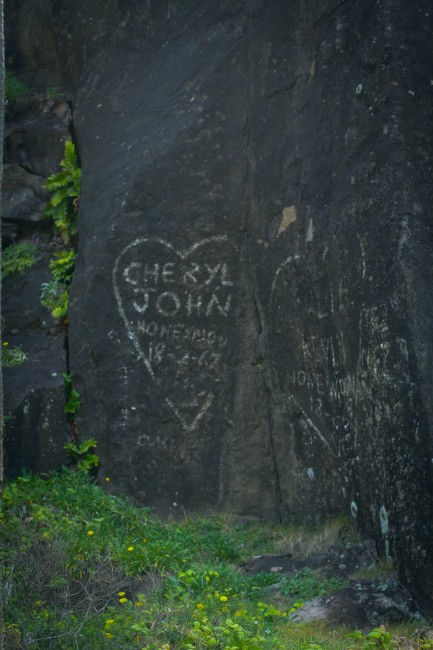 Photo of white painted graffiti on a rock face that says "CHERYL JOHN HONEYMOON 8-2-67" with a heart around the words.