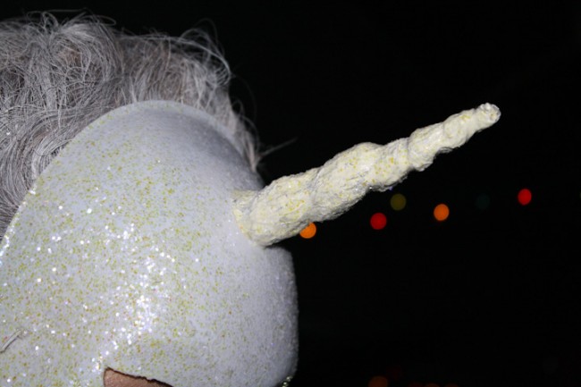 Close up photo of a white mask with a horn with glitter all over it.