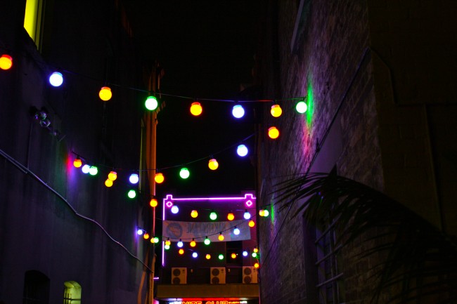 Photo of colourful lights strung between buildings over an alleyway.