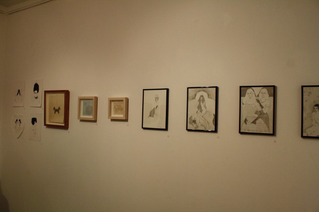 Photo of a bunch of small framed artworks lined across a white wall.