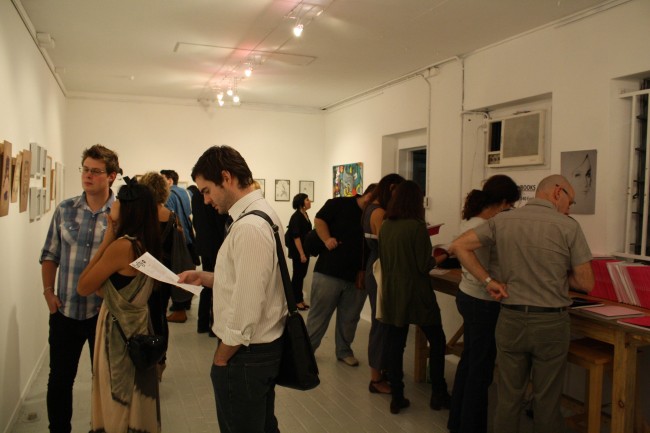 Photo of a crowd of people milling about inside a small gallery with white walls.
