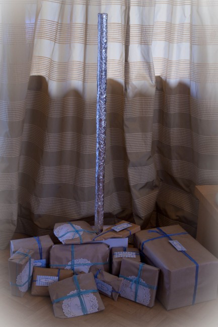 Photo of a pole wrapped in tin foil and standing up with brown paper wrapped presents at the bottom of it.