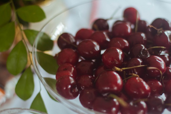 Close up photo of shiny red cherries sitting in a clear bowl.