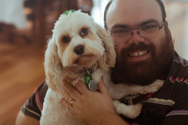 Photo of Nick, a bearded pale skinned man with glasses, holding Molly the dog whi is white and fluffy and looking at the camera dolefully.