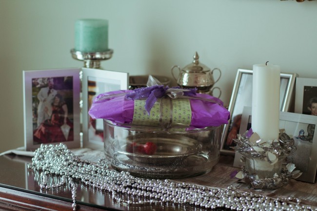 Photo of lots of photo frames, silver trinkets and a purple wrapped present sitting on a sideboard.
