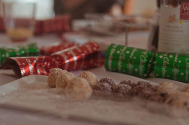 Photo of some apricot and rum balls on the table with some red and green shiny bon bons sitting behind the plate.