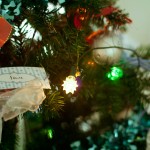 Close up photo of Mum's green christmas tree with lights and baubles and the little gift card I drew for my brother Sam hanging in the branches.