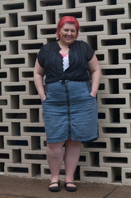 Outfit photo of me (with pink short hair!) wearing a black and white polka dot shirt over a white singlet tucked into a high waisted blue skirt with a zip up the centre. My hands are in the pockets of my skirt.