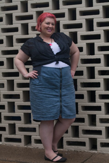 Outfit photo of me (with pink short hair!) wearing a black and white polka dot shirt over a white singlet tucked into a high waisted blue skirt with a zip up the centre. My hands are on my hips and I'm grinning.