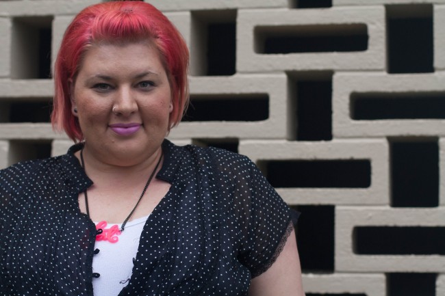 A head and shoulders photo of me, wearing a black shirt with polka dots over a white singlet with a pink fat necklace. I'm wearing awesome pale pink lipstick!