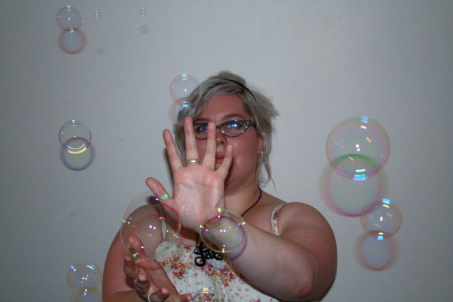 Photo of Zoe holding her hand up, seemingly pushing back a bunch of bubbles floating past her.