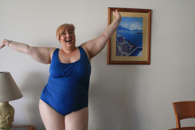 Photo of me wearing a blue swimsuit with my arms thrown in the air and a joyful grin on my face.