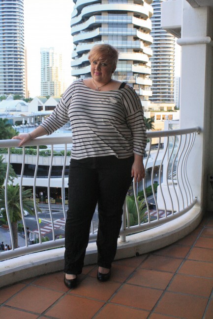 Outfit photo of me standing on a balcony wearing a black and white striped tee with black jeans.
