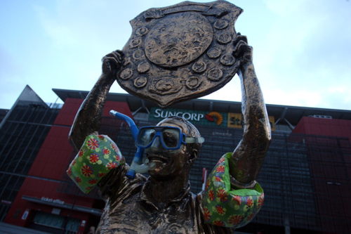 Photo of the statue of Wally Lewis, a rugby league hero in Australia; he holds up a shield full of awards. Someone has added inflatable floaties around his upper arms, and some goggles and a snorkle to his face.