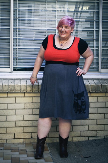 Outfit photo of me standing in front of a window with my hand on my hip. I'm wearing a black tshirt under a dress with a red top, black under bust band and grey skirt with an OWL on the bottom! Also brown cowboy boots. 