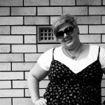 Photo of me standing against a brick wall, hands on hips and smiling.