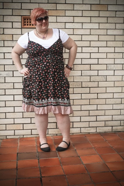 Outfit photo of me, light skinned fat lady with short lilac hair, standing in front of a brick wall. I'm wearing a dark floral sundress with a white short sleeved tshirt underneath with black mary jane crocs.