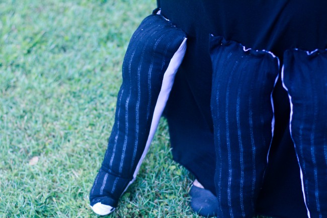 Photo of a couple of stuffed toy-like tentacles attached to the bottom of my skirt. The tops is a black fabric with a pin stripe and you can see underneath there's hints of purple fabric.