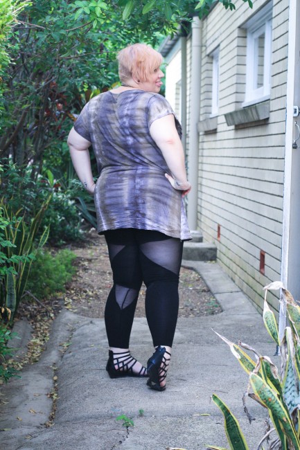 Outfit photo of me, a fat pale skinned lady, posing with both my hands on my hips with my butt facing the camera. I'm wearing a purple and grey tie dyed tshirt with black leggings with sheer cut outs.