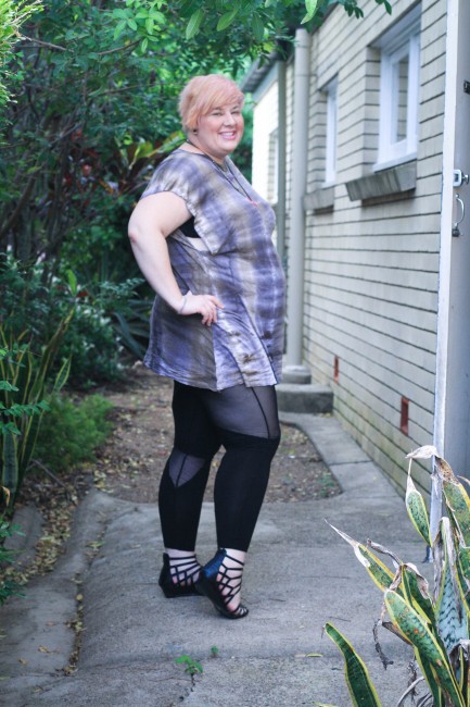 Outfit photo of me, a fat pale skinned lady, posing side on with my hand on my hip. I'm wearing a purple and grey tie dyed tshirt with black leggings with sheer cut outs as well as a pink fat necklace.