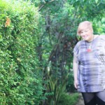 Photo of me, out of focus, standing next to a green hedge, which is in focus,