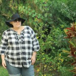 Photo of me standing in the garden wearing a black and white tartan tunic with shorts and a big black hat.