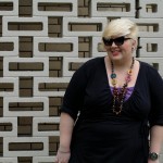 Photo of my upper half wearing a black wrap dress with a purple camisole underneath and a multicoloured bead necklace with black pointy silver tipped sunglasses.