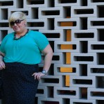 Photo of me standing in front of a brick wall wearing a green tshirt with a black and grey leopard print pencil skirt.