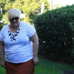 Photo of me in the garden wearing a white t-shirt with black and white fabric flowers around the neckline and a rust skirt.