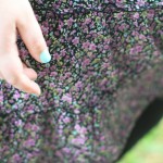 A photo of my hand with a polish colour that sits between Tiffany Blue and turquoise against my skirt which is a small purple and green floral print.