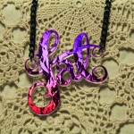 A photo of a fat necklace made out of purple hologram acrylic on black chain against a crocheted background.