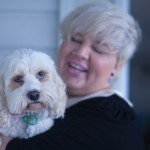 A photo of me holding a long haired small white dog. She has a solomn look on her face while I'm laughing.