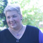 A photo of my head and shoulders, my hair is pinned up and I'm wearing two purple stone necklaces. I'm looking to the side and smiling a bit.