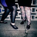A photo of Zoe and my fat legs. On the left, Zoe's leggings are sheer black in front and solid at the back and she wears slip on shoes with cross over elastic. I wear floral tights with black platform heels.