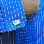 A close up photo of Nick's pinstriped shirt cuffs, secured with cuff links with a gem in them, and his blue paisley tie.