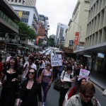 A photo looking towards the marchers. One sign sticks out and it says "Ask. Listen. Respect."