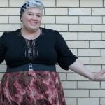 A photo of me from the waist up wearing a black elbow length dress as a top with a lace detail down the front, and a red paisley skirt work on my high natural waist with a black belt.