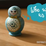 A photo of the nesting doll with all dolls packed away inside. It's painted turquoise and white with gold accents and paisley motifs. Hand lettering in a thought bubble says, "Who won us?"