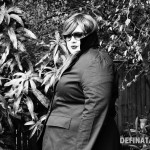 A photo of Natalie from the side peeking from behind the turned up collar of the jacket.