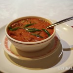 A bowl of bright red soup in a small bowl with beans and tofu.