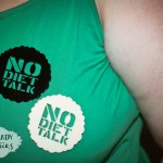 A photo of two No Diet Talk brooches in black and ivory pinned to my green singlet.